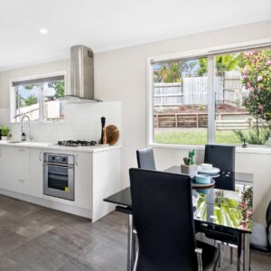 White kitchen with black dining table, and stone coloured tile flooring.