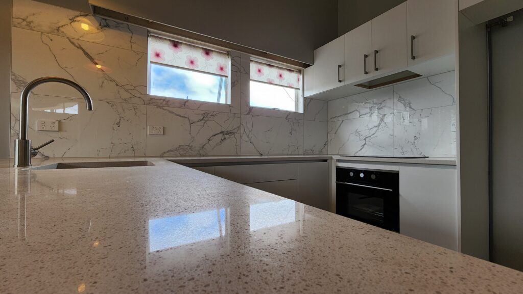 Kitchen with tiled backsplash stone benchtop and white cabintry.